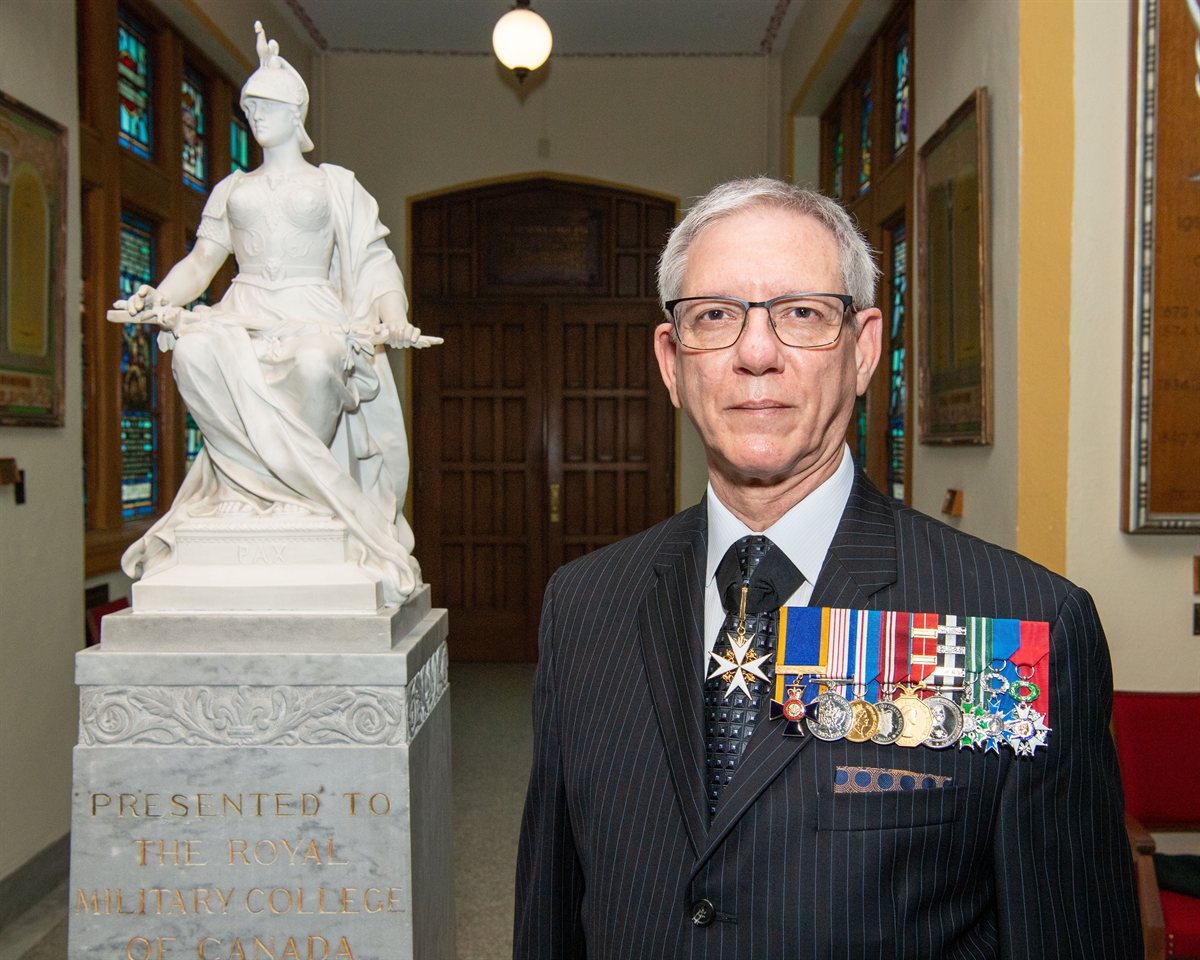 Dr. André M. Levesque in formal dress with medals, beside the Pax statue at the Royal Military College of Canada